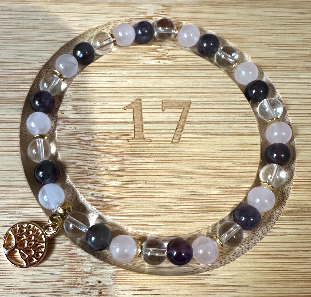 Bracelet en Quartz Rose, Améthyste et Cristal de Roche, orné d’un pendentif arbre de vie doré. Présenté sur un support en bois gravé, il allie élégance et énergie apaisante.